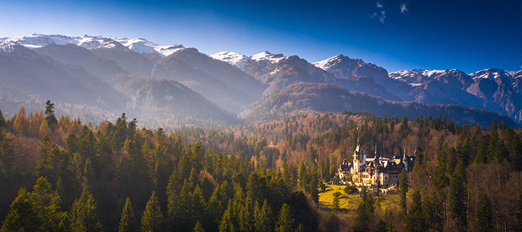 Peles Castle lit up by sun rays amid mountains and forest, like a fairy tale.