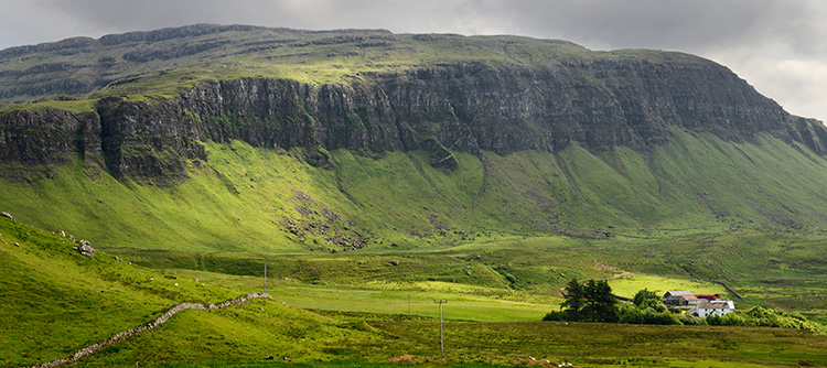A farmstead on the Isle of Mull is dwarfed by beautiful, grassy cliffs.